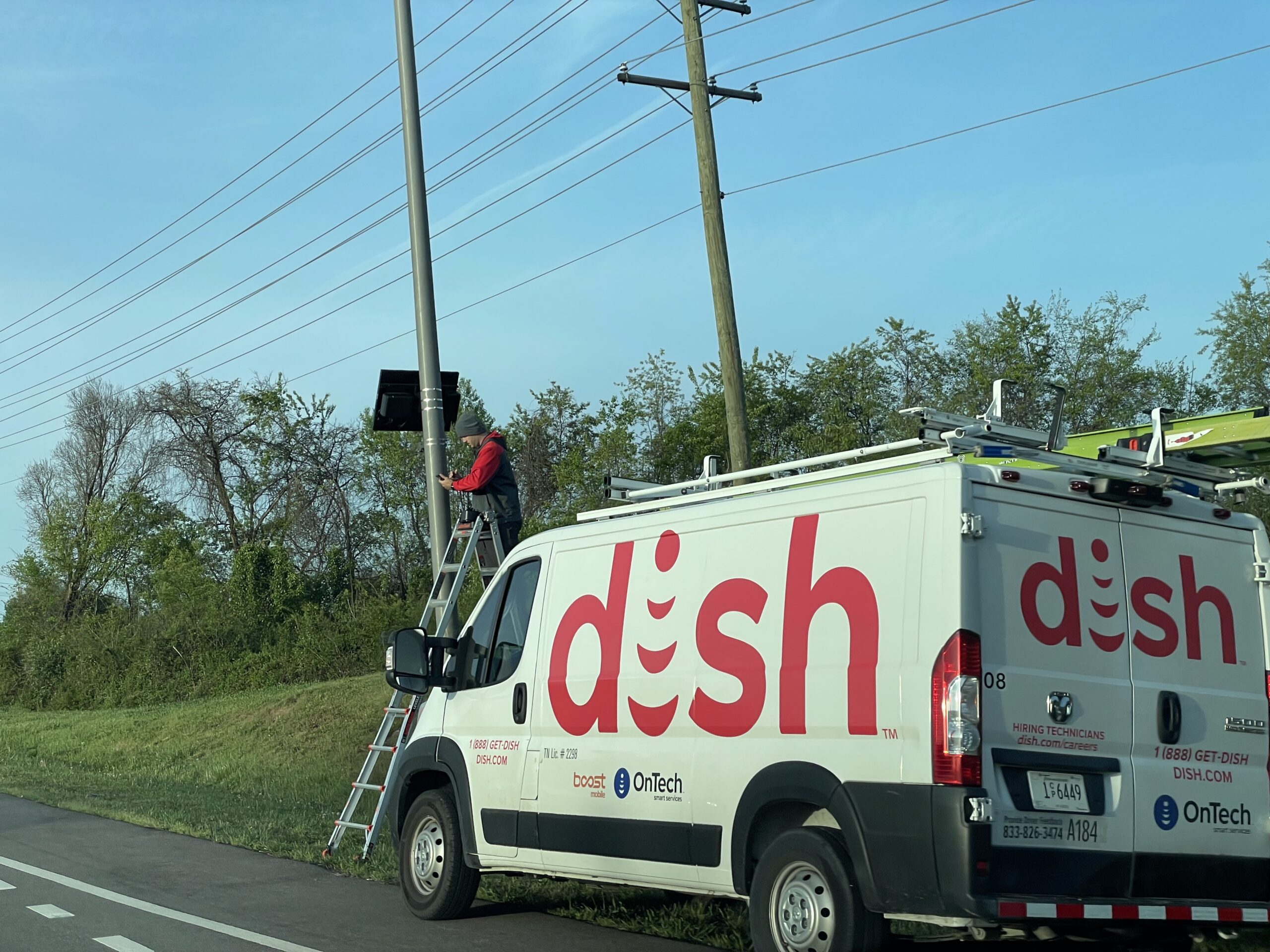 Dish Network-branded van beside a pole-mounted Flock Safety surveillance camera in Maryville, Tennessee, April 6, 2026
